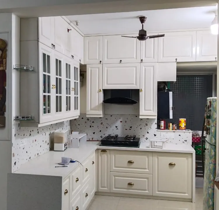 European-style white shaker L-shaped modular kitchen with terrazzo backsplash by Bella Kitchens, Pune